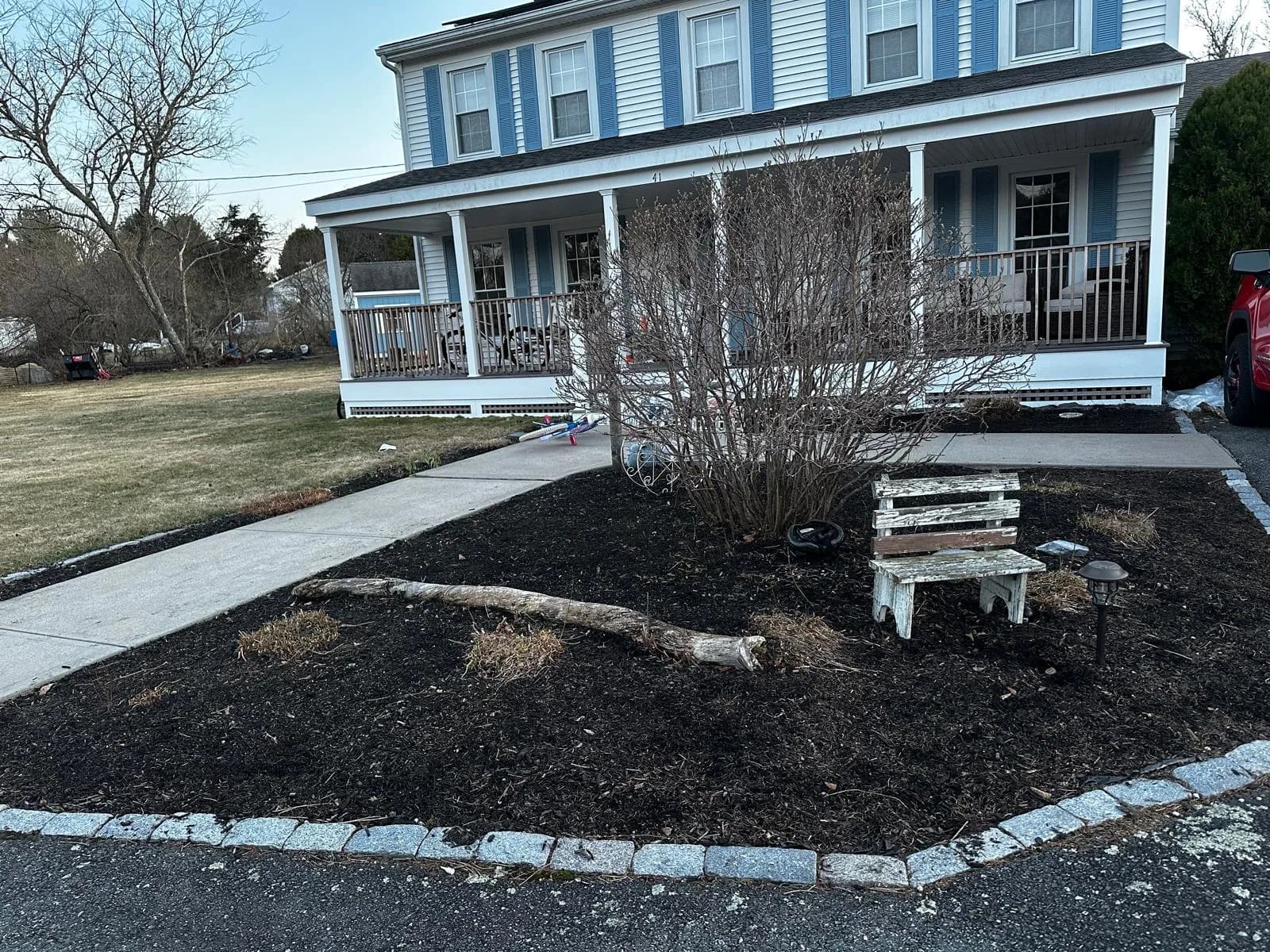 An Aldo Unlimited residential fall cleanup result — fresh-mulched foundation beds in front of a blue-and-white coastal home, sidewalk swept, beds ready for winter.
