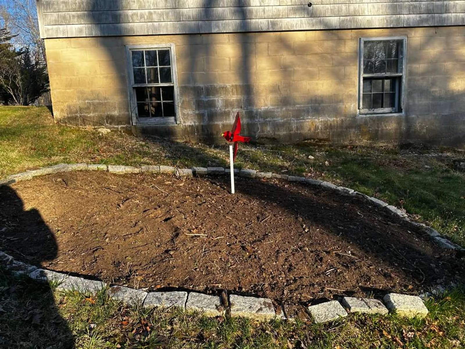 An Aldo Unlimited stone-edged foundation bed in Stonington, CT — granite cobble edging against weathered shake siding, freshly turned soil.