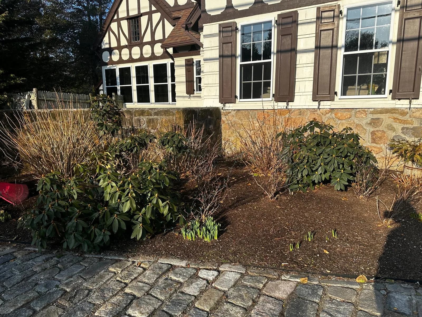 An Aldo Unlimited Tudor-style home in Westerly, RI — refined foundation-bed work with a stone wall and slate paver walkway.