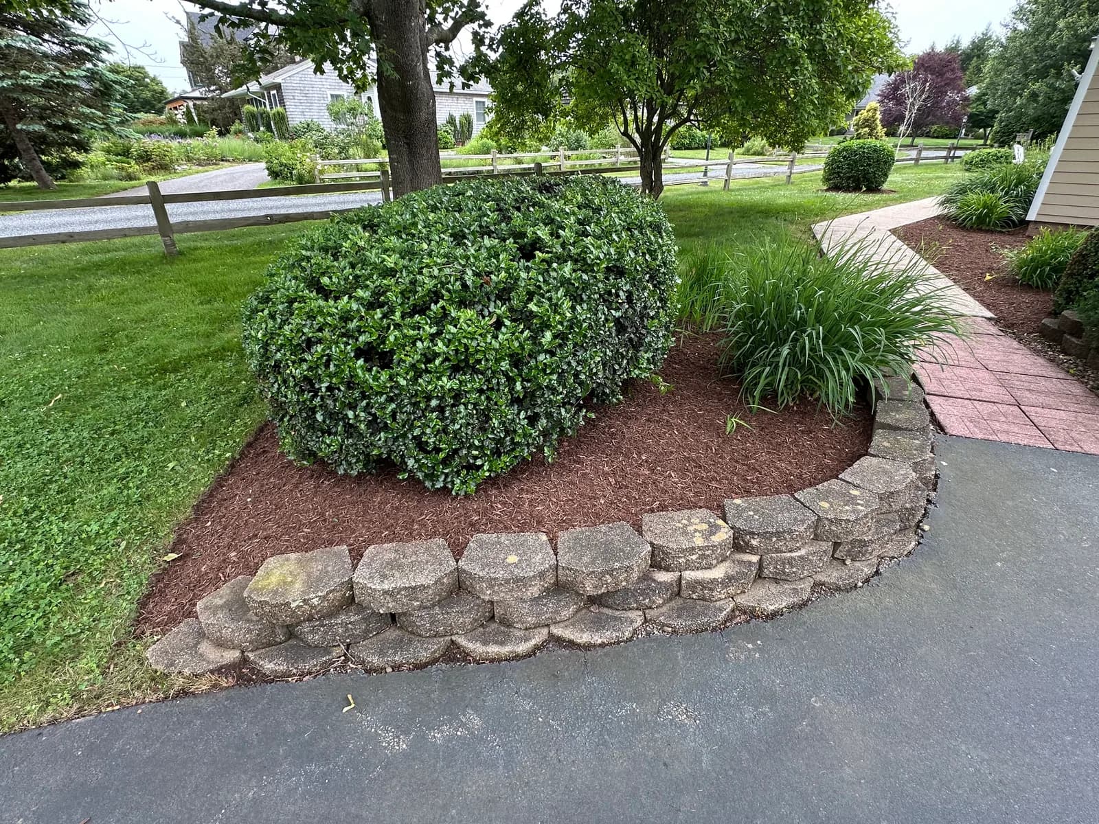 A refined Aldo Unlimited front yard — sculpted hedge, fresh mulch bed over a stone wall, edged driveway, lush green lawn.